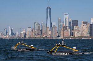 Two XOCEAN USVs swimming on the surface of the ocean with the New York skyline in the background.