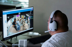 a doctor with a headset sits in front of a monitor showing a surgery in an operating room.